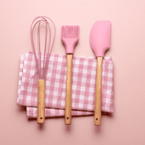 "Set of pink baking tools including whisk, spatula, and pastry brush on checkered cloth"