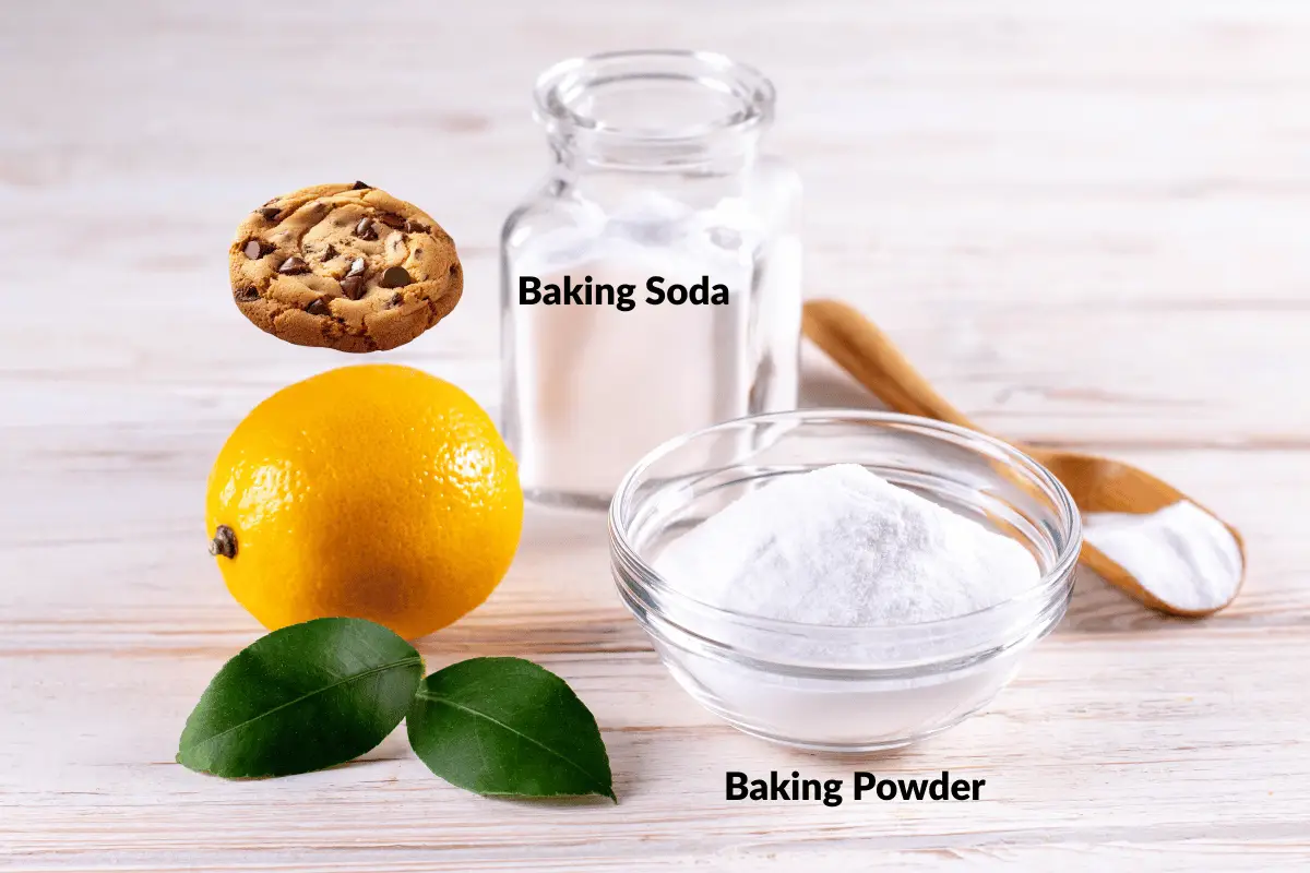 Baking soda vs baking powder in cookies, labeled jars and bowls on a light wood background with lemon and cookie for context