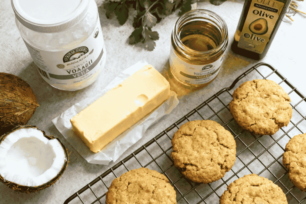 Vegan baking setup with coconut oil, vegan butter, avocado oil, and olive oil beside golden-brown cookies cooling on rack — highlighting plant-based fat options.